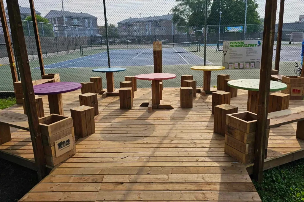 Terrasse en bois animée par des tables rondes colorées près d'un terrain sportif