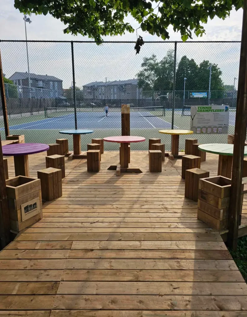 Tables rondes colorées sur terrasse en bois près d'un terrain de sport