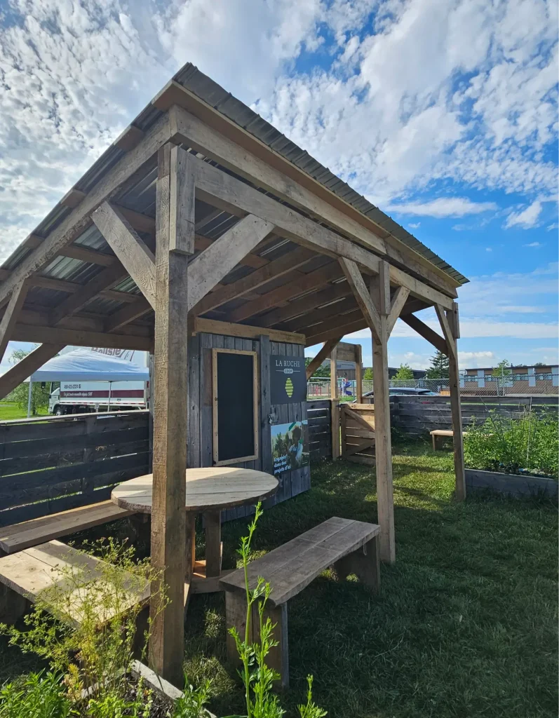 Structure en bois abritant table ronde et bancs dans un jardin communautaire