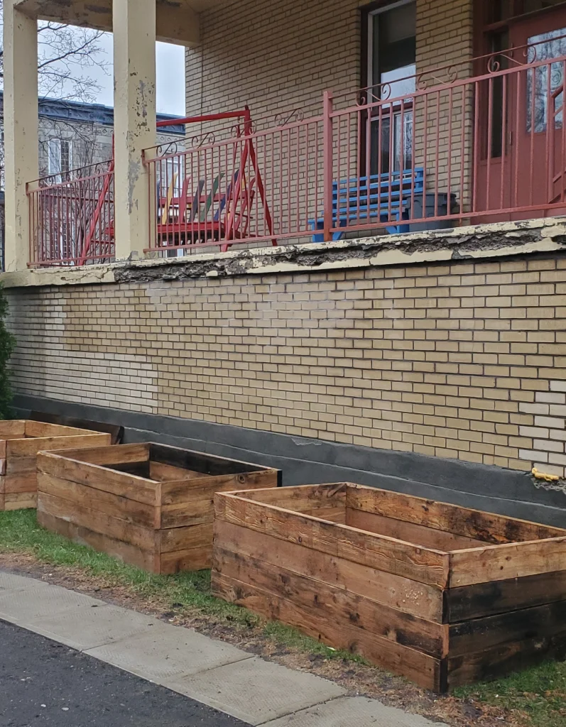 Trois bacs en bois vides alignés devant mur de briques à Montréal