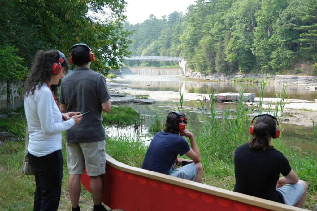 Groupe avec audioguides près d’un canot rouge au bord de la rivière