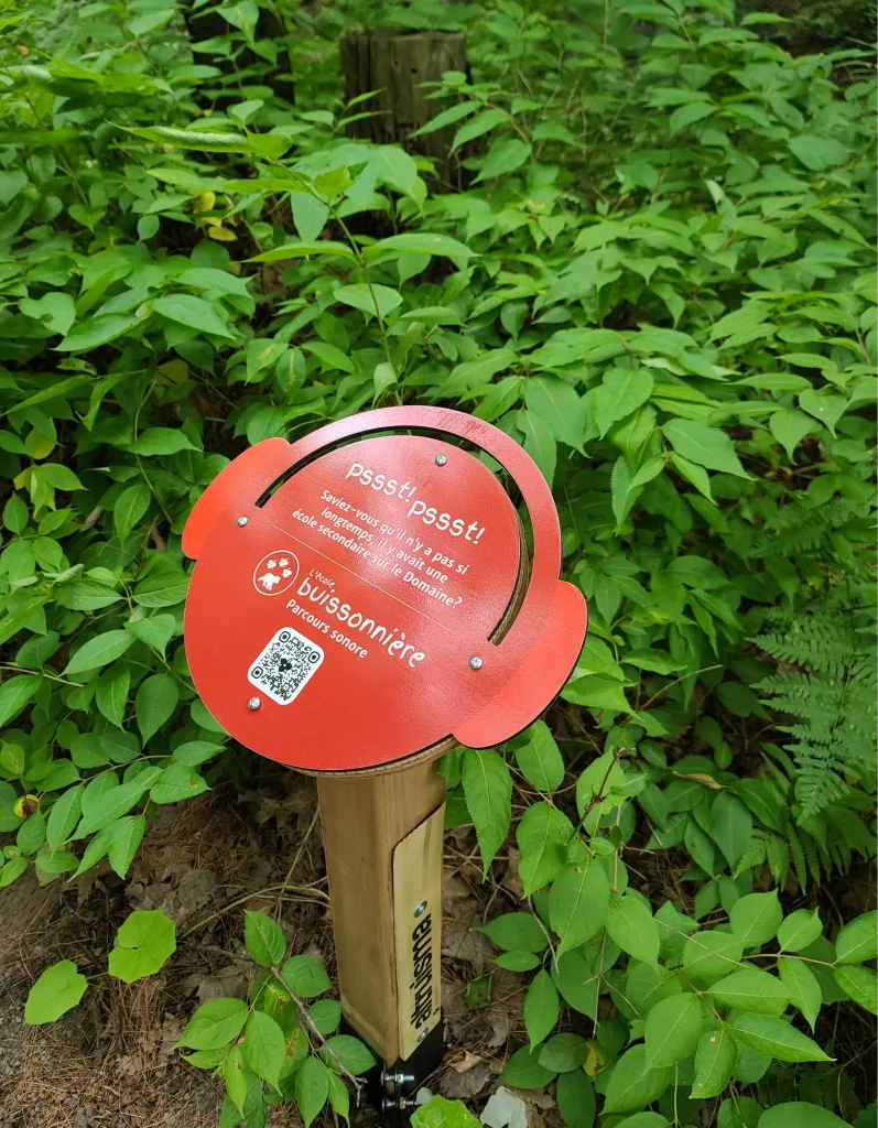 Plaque rouge avec code QR du parcours sonore, en pleine forêt
