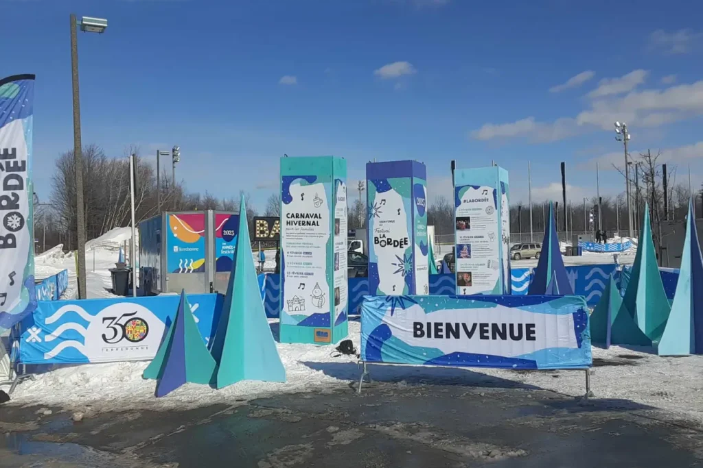 Ensemble de colonnes d’info et bannières « Bienvenue » structurant l’entrée du site hivernal à Terrebonne.